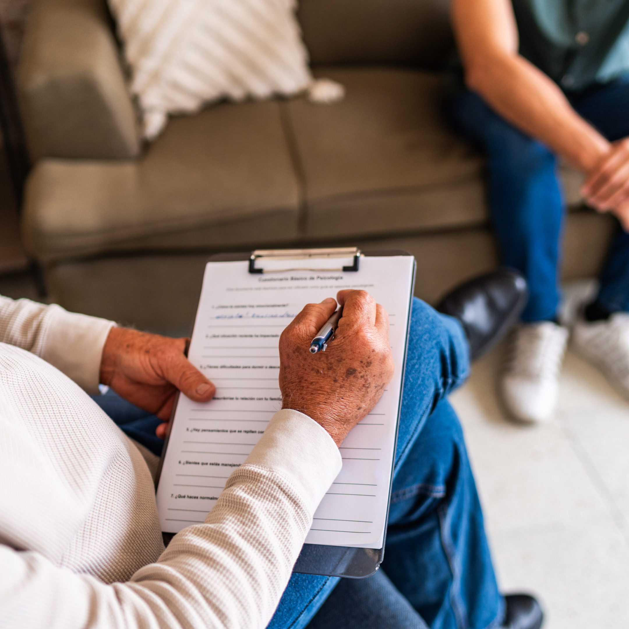 Close-up of psychotherapist man writing on clipboard during therapy session at clinic